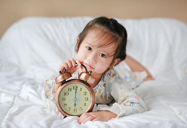 Schattig meisje wordt wakker in de ochtend met wekker op bed