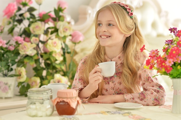 Schattig meisje zit aan tafel en drinkt thee