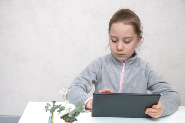 Schattig meisje zittend aan tafel werkt in de tablet online leren