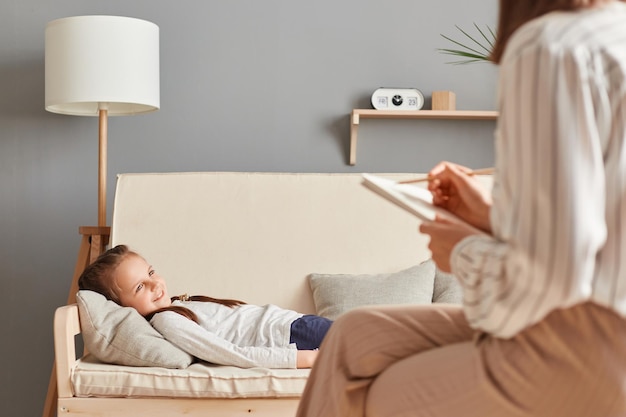 Schattig ontspannen klein meisje liggend op de bank in psychologisch kantoor met overleg met arts-specialist kinderen depressie benadrukt kind huiselijk geweld