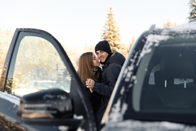 Schattig paar knuffelen in de buurt van auto in de winter man en vrouw verliefd kijken elkaar aan in de buurt van de auto