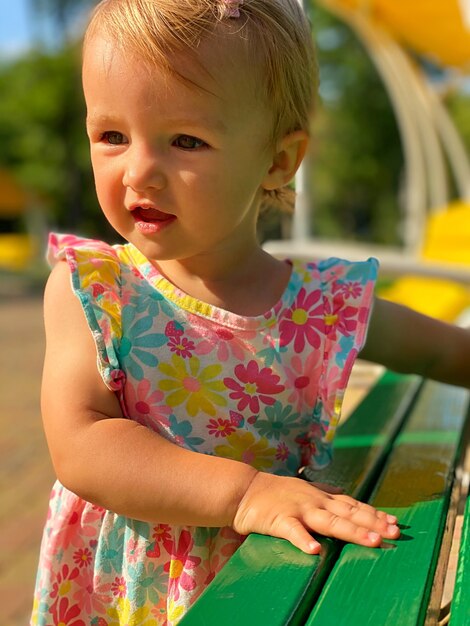 Schattig peutermeisje in jurk met bloemenprint die wegkijkt naar de zomertijd in het park