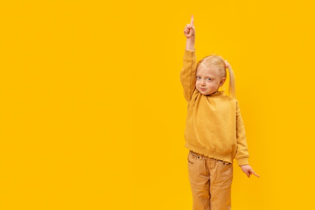 Schattig preschool meisje in geel pak stak haar hand op en wijst vinger omhoog en wijst naar beneden met haar andere hand Kopieer ruimte mock up
