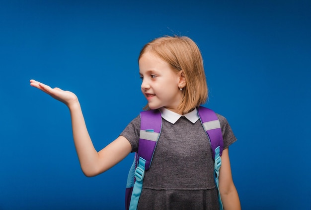 Schattig schoolmeisje meisje kijkt naar haar handpalm op een blauwe achtergrond