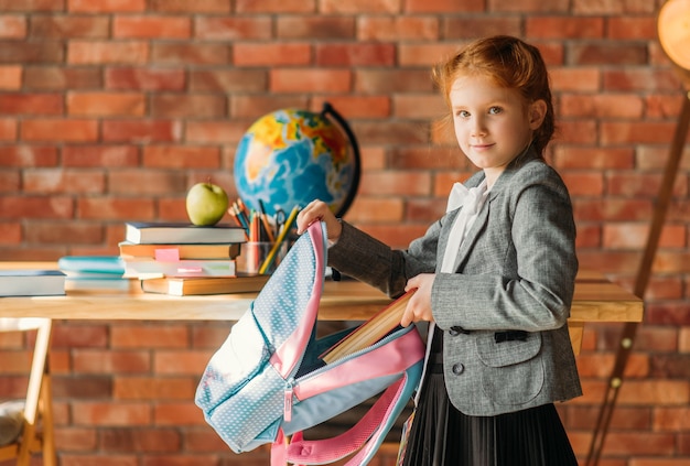 Schattig schoolmeisje zet leerboek in de Schooltas, zijaanzicht.