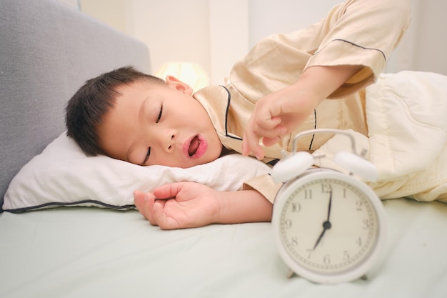 Foto schattig slaperig klein kind dat op het bed ligt en stopt met het uitschakelen van de wekker in de slaapkamer thuis