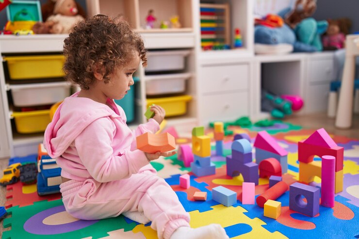 Schattig Spaans meisje speelt met bouwblokken zittend op de vloer op de kleuterschool