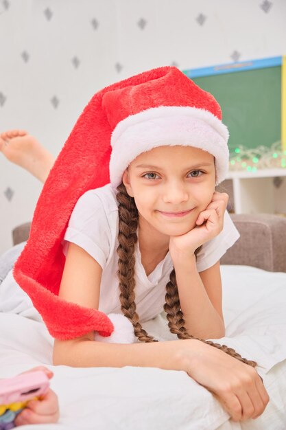 Schattig tienermeisje bruinharig in kerstman hoed ligt op het bed in de kinderkamer