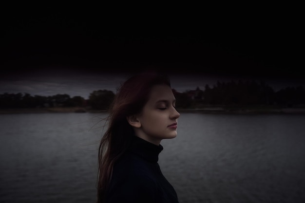 Schattig tienermeisje dat haar ogen sluit, geniet 's avonds buiten van de frisse lucht aan het water