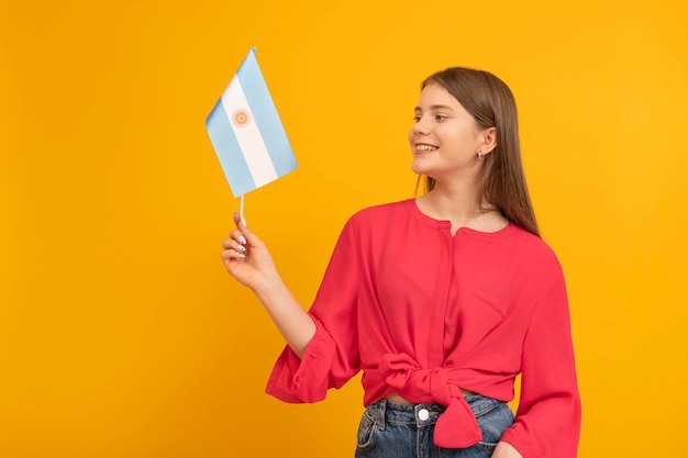 Schattig tienermeisje houdt de vlag van Argentinië op oranje achtergrond Jeugd in Argentinië Reis naar Zuid-Amerika