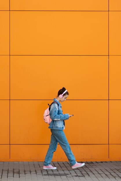 Schattig tienermeisje met een gadget en koptelefoon tegen de achtergrond van een oranje muur