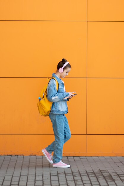 Schattig tienermeisje met een gadget en koptelefoon tegen de achtergrond van een oranje muur