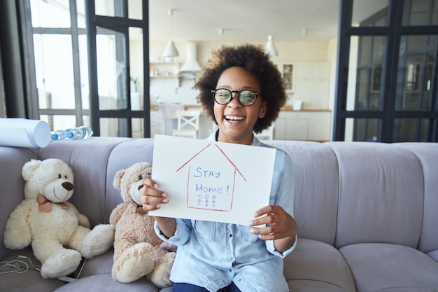 Schattig tienermeisje van gemengd ras in vrijetijdskleding die er gelukkig uitziet terwijl ze thuis blijft tekenen terwijl ze zit