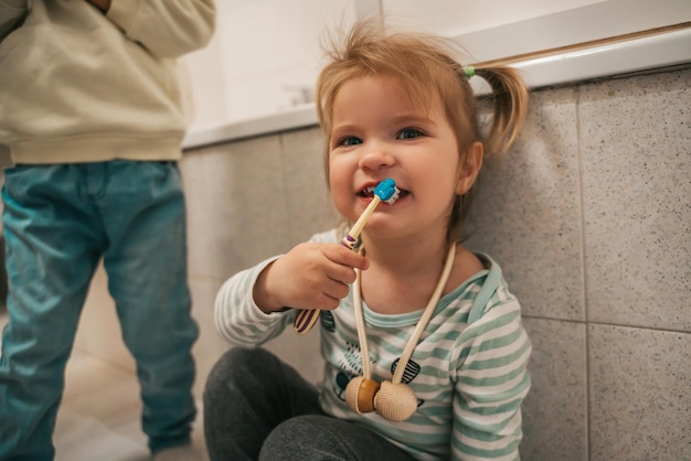 Schattig vrouwelijk kind dat in de badkamer zit en haar tanden poetst in aanwezigheid van haar broer of zus