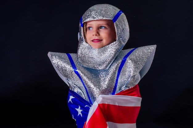 schattig vrouwelijk kind in kostuum helm spelen heldere folie zilveren kosmonaut in uniform met Amerikaanse vlag zwarte achtergrond in de studio.patriottisme 20 juli 1969 landing op de maan concept ruimtedag