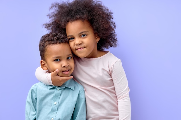 Schattig zwart meisje knuffelen broertje, liefde en genegenheid, paarse studio achtergrond tonen. gelukkig liefdevolle afro-amerikaanse broers en zussen in vrijetijdskleding omarmen en glimlachen naar de camera. familie liefde