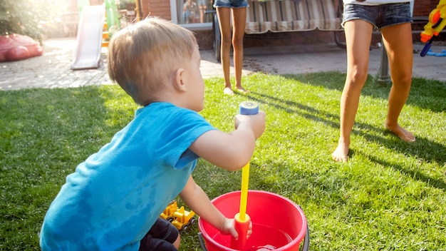 Foto schattige 3 jaar oude peuterjongen die water opspat uit plastic speelgoedgeweer in de achtertuin van het huis. kinderen die in de zomer buiten spelen en plezier hebben