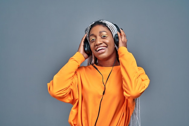 Schattige Afro-Amerikaanse lachende vrouw in geel shirt luisteren naar muziek met behulp van draadloze oortelefoons