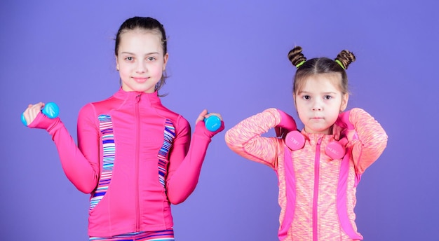 Schattige atleten Kleine kinderen die fysieke fitheid ontwikkelen Kleine meisjes genieten van fitnesstraining met gewichten Schattige zussen die fitnessoefeningen in de sportschool doen met halters Sport en fitness voor kinderen