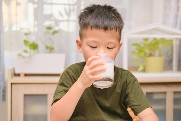 Schattige Aziatische 5 jaar oude kleuterschool jongenskind melk drinken uit een glas Klein kind zit en glas melk vast te houden bij het ontbijt in de ochtend thuis Beste drankjes voor kinderen concept