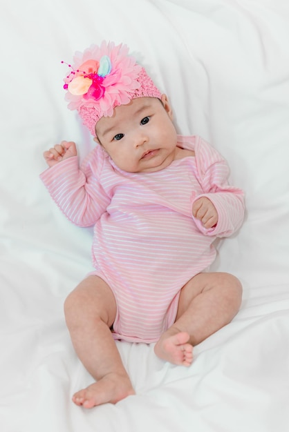 Schattige Aziatische babymeisje Zit op het bed in roze jurk