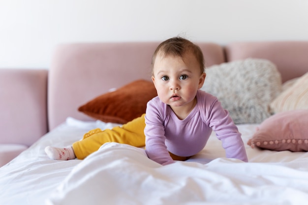 Schattige baby die op het bed kruipt en er verbaasd uitziet