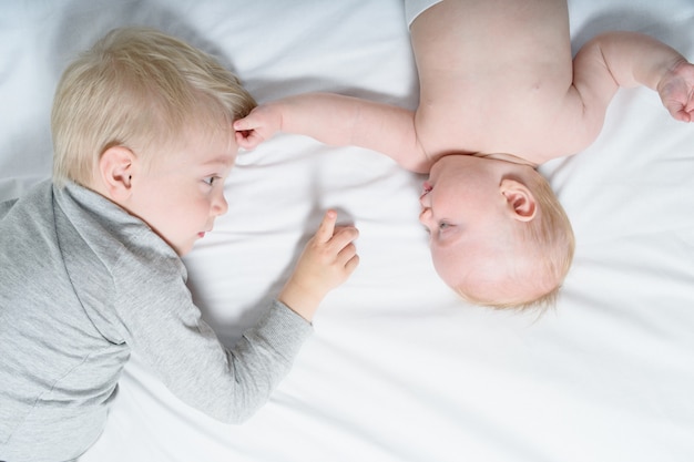 Schattige baby en oudere broer werken samen terwijl ze op het bed liggen