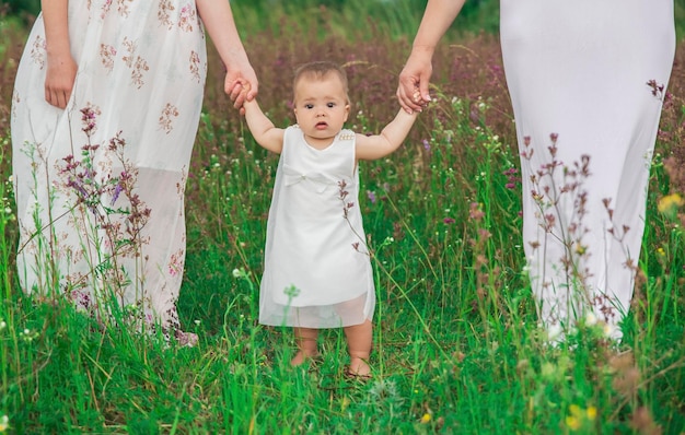 schattige baby in avondjurk houdt handen vast van moeder en oudere zus