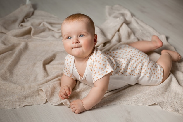 Schattige baby in een bodysuit ligt op zijn buik op de houten vloer met een deken thuis