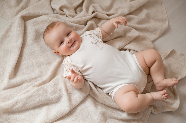 Schattige baby in een bodysuit ligt op zijn rug op de houten vloer met een deken thuis