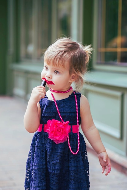 Schattige baby in een jurk schildert lippen met lippenstift