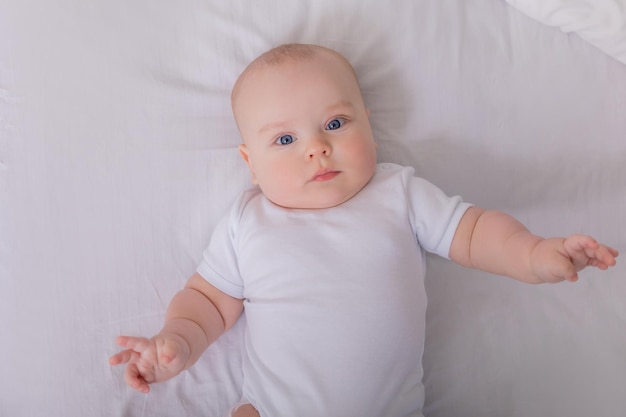 Schattige baby in een witte Romper liggend in bed met katoenen ondergoed bovenaanzicht ruimte voor tekst