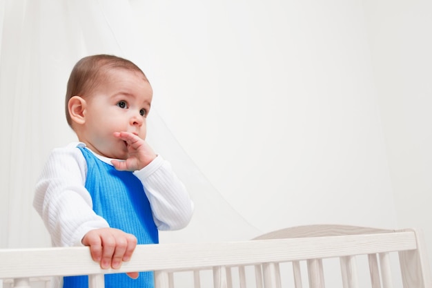 Schattige baby in het bed op een witte achtergrond, kijk naar één kant met de vinger in de mond