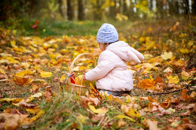 Schattige baby in jas zit in herfstbos speelt met pompoen gouden herfst en Halloween-feest