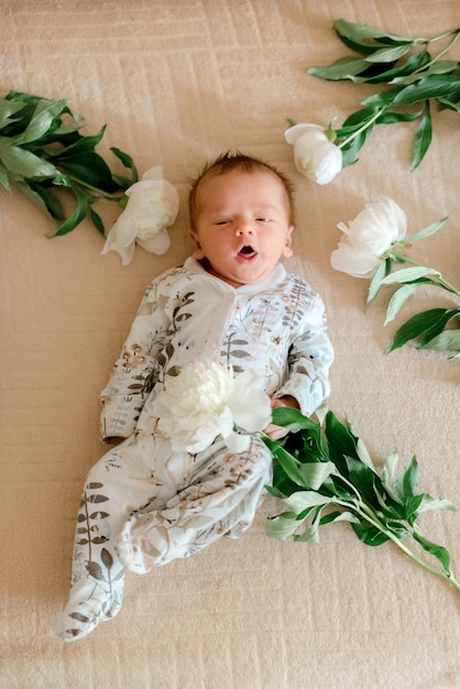 Schattige baby in met bloemen bedrukte kleding die in pioenrozen ligt