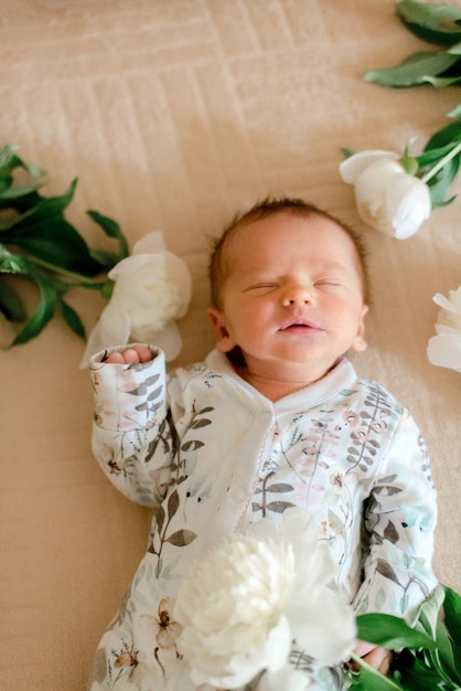 Schattige baby in met bloemen bedrukte kleding die in pioenrozen ligt