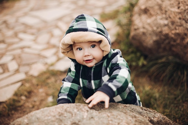 Schattige baby in warme overall met capuchon zittend op gebladerte