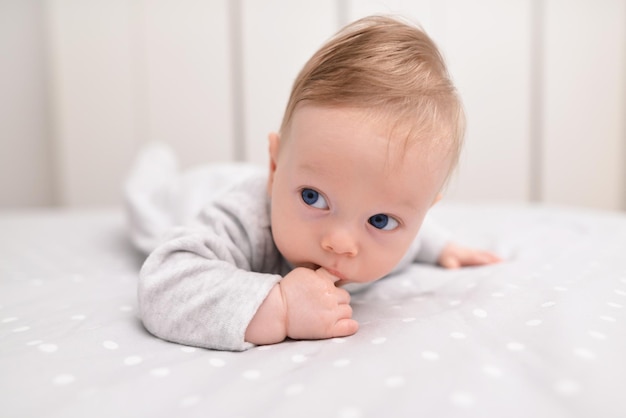 Schattige baby liggend op een wit laken en houdt vingers in zijn mond Gelukkig jeugdconcept