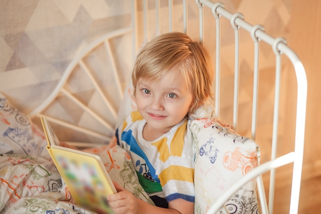 Schattige baby ligt in bed en leest een boek.