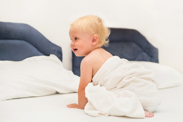 Schattige baby onder een witte handdoek zit op het bed