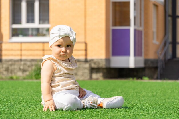 Schattige baby peuter zittend op een groen gazon op de achtergrond van het huis