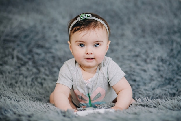 Schattige baby van zes maanden oud die zich op grijs zacht blad met haar handen bevindt