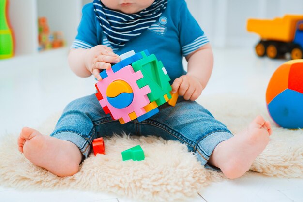 Foto schattige baby zit op de vloer van het huis te spelen met kleurrijk educatief speelgoed