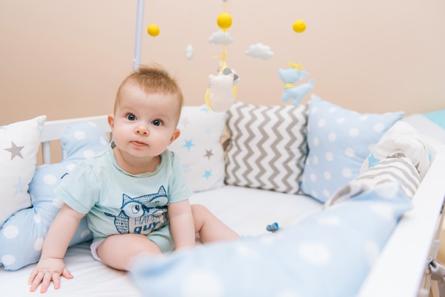 Schattige baby zitten in een witte ronde bed. Licht kinderdagverblijf voor jonge kinderen. Speelgoed voor kinderbedje. Het glimlachende kind spelen met mobiel van vilt in zonnige slaapkamer.