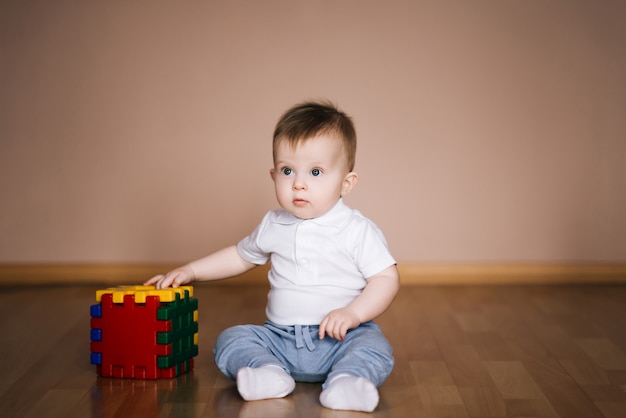 Schattige baby zittend op de vloer van het huis spelen met een veelkleurige kubus