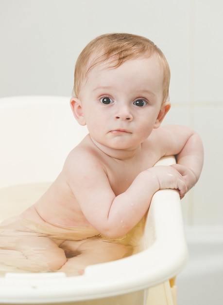 Schattige babyjongen baden en kijken naar de camera