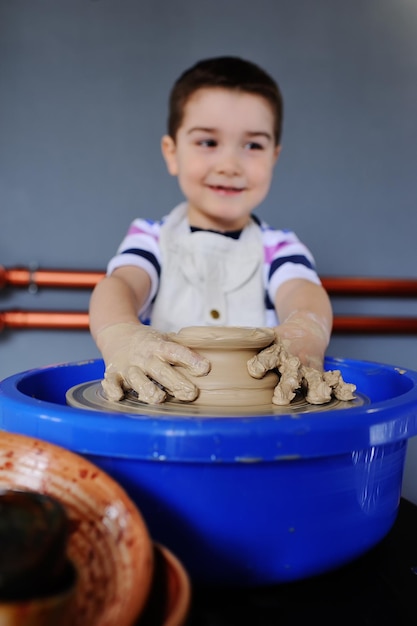 Schattige babyjongen beeldhouwt uit kleikom op een pottenbakkersschijf