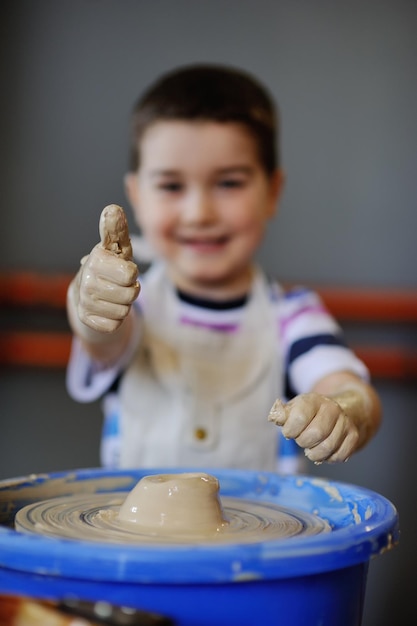 Schattige babyjongen beeldhouwt uit kleikom op een pottenbakkersschijf