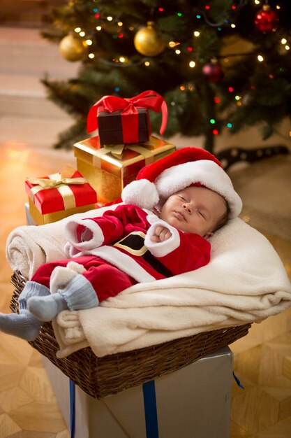 Schattige babyjongen in kerstmankostuum die onder de kerstboom slaapt