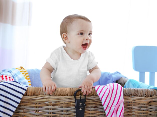 Schattige babyjongen in rieten mand met kleren